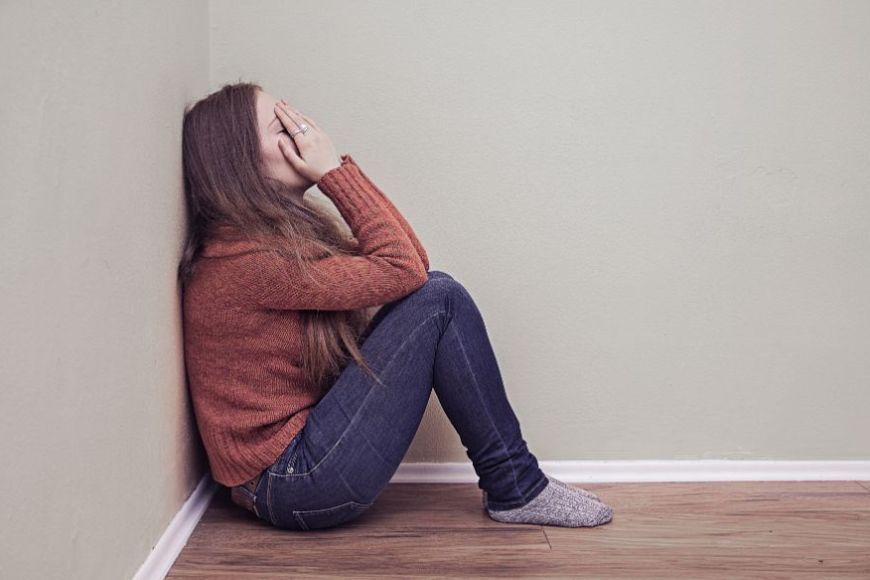 Una noia asseguda en un racó tapant-se la cara Una noia asseguda en un racó tapant-se la cara