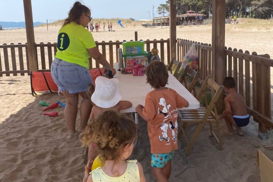 Una monitora i diversos nens i nenes jugant al Mini Beach Club de l'Estartit Una monitora i diversos nens i nenes jugant al Mini Beach Club de l'Estartit